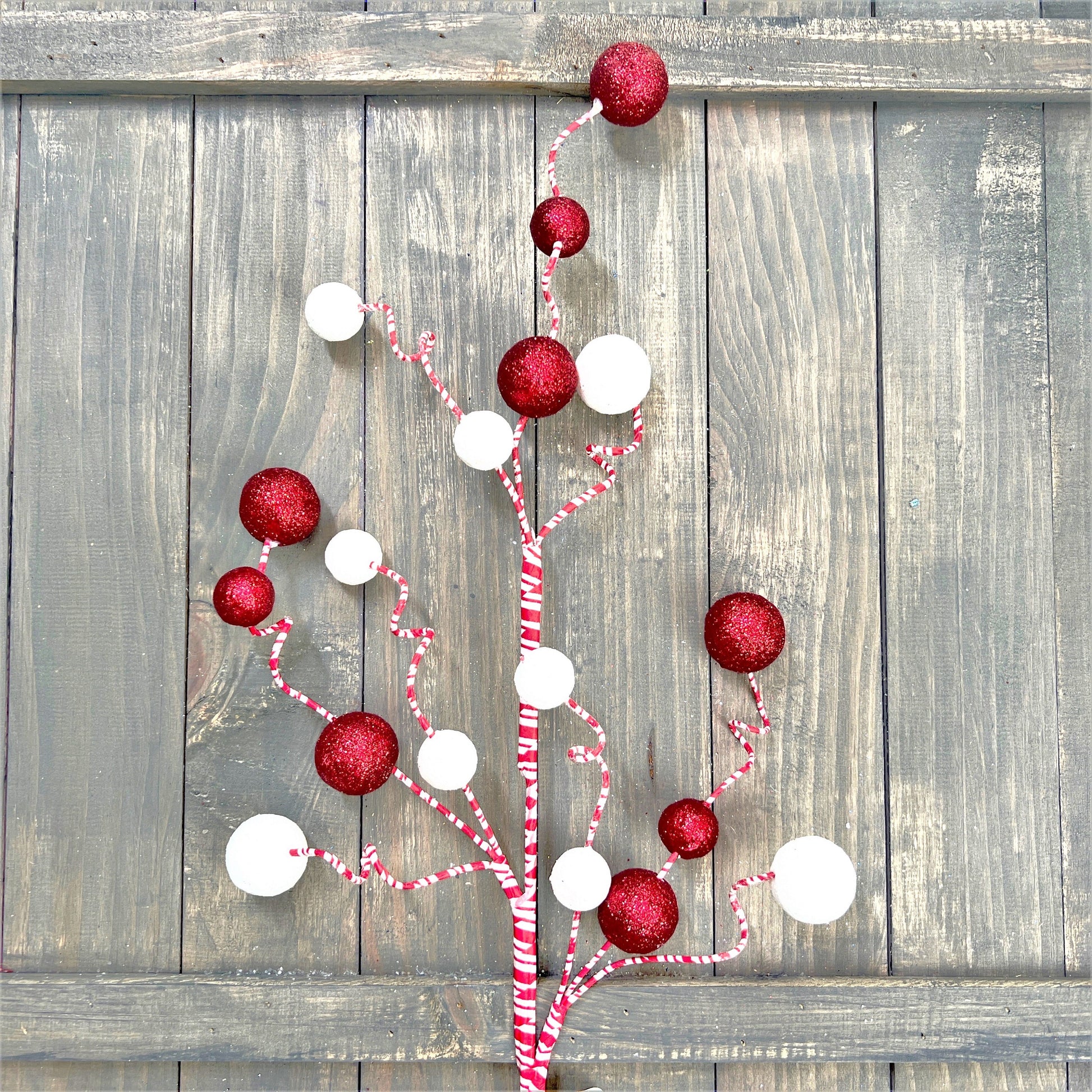 A 31 inch peppermint glitter ball spray rests against a distressed wood fence.