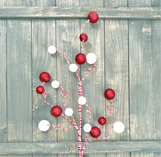 A 31 inch peppermint glitter ball spray rests against a distressed wood fence.